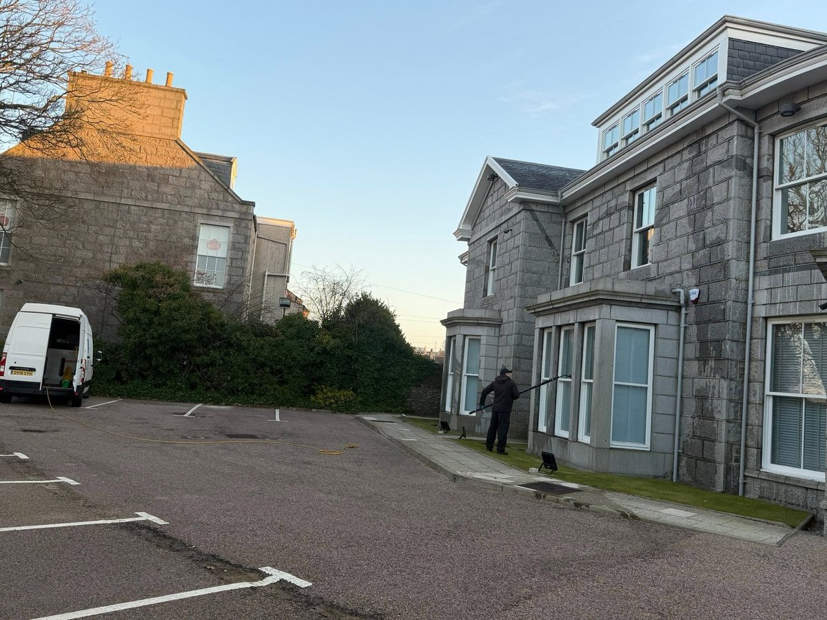 Two stone buildings on either side of a driveway with a white van parked on the left, clear sky above