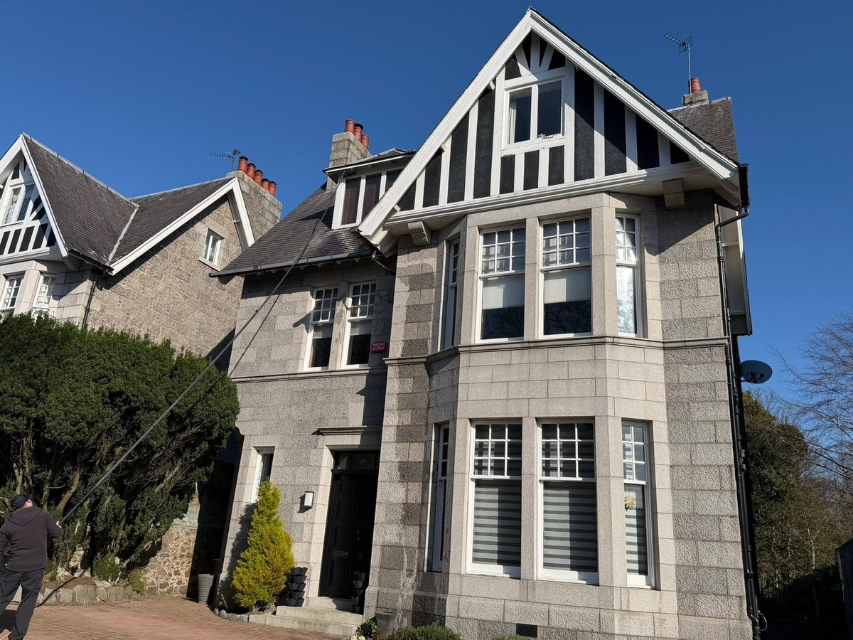 Scottish stone manor house with black and white gables, multi-level windows, and ivy-covered walls against a blue sky